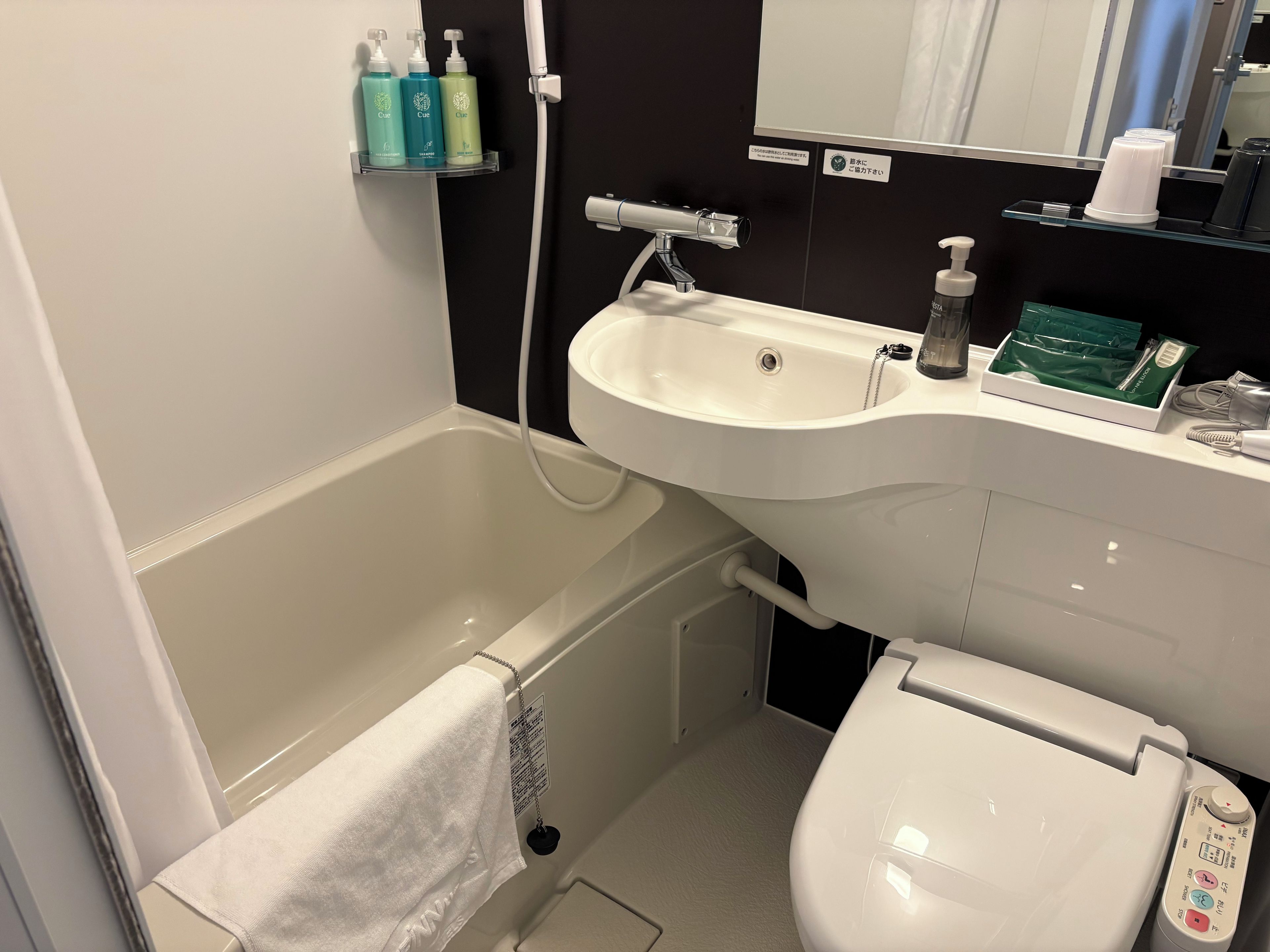 A bathroom with a bathtub, a sink, and a toilet. There are toiletries on the sink and a towel hanging on the wall.