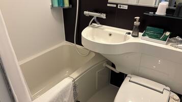A bathroom with a bathtub, a sink, and a toilet. There are toiletries on the sink and a towel hanging on the wall.