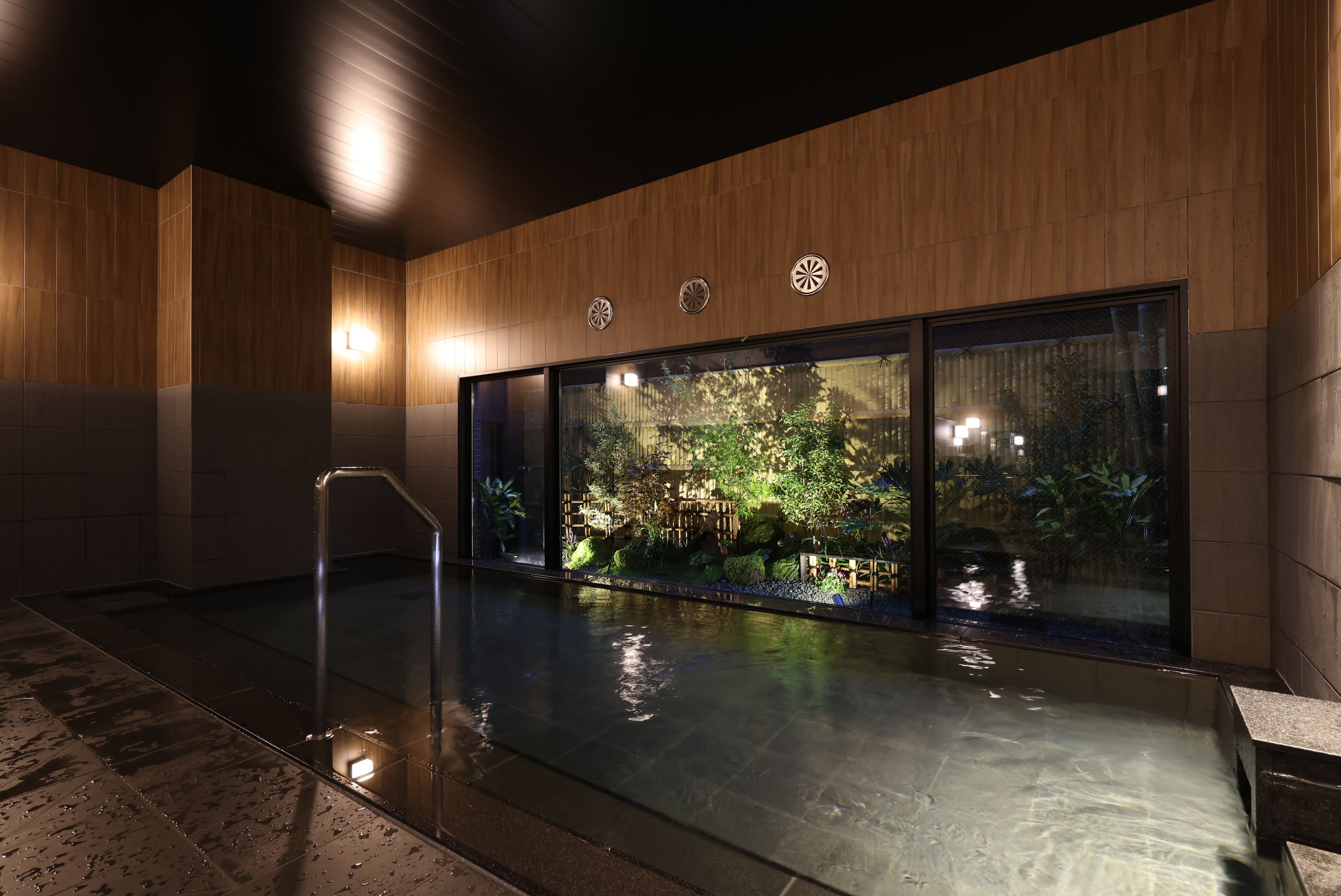 A modern indoor pool area with a glass wall, wooden paneling, and a metal handrail.