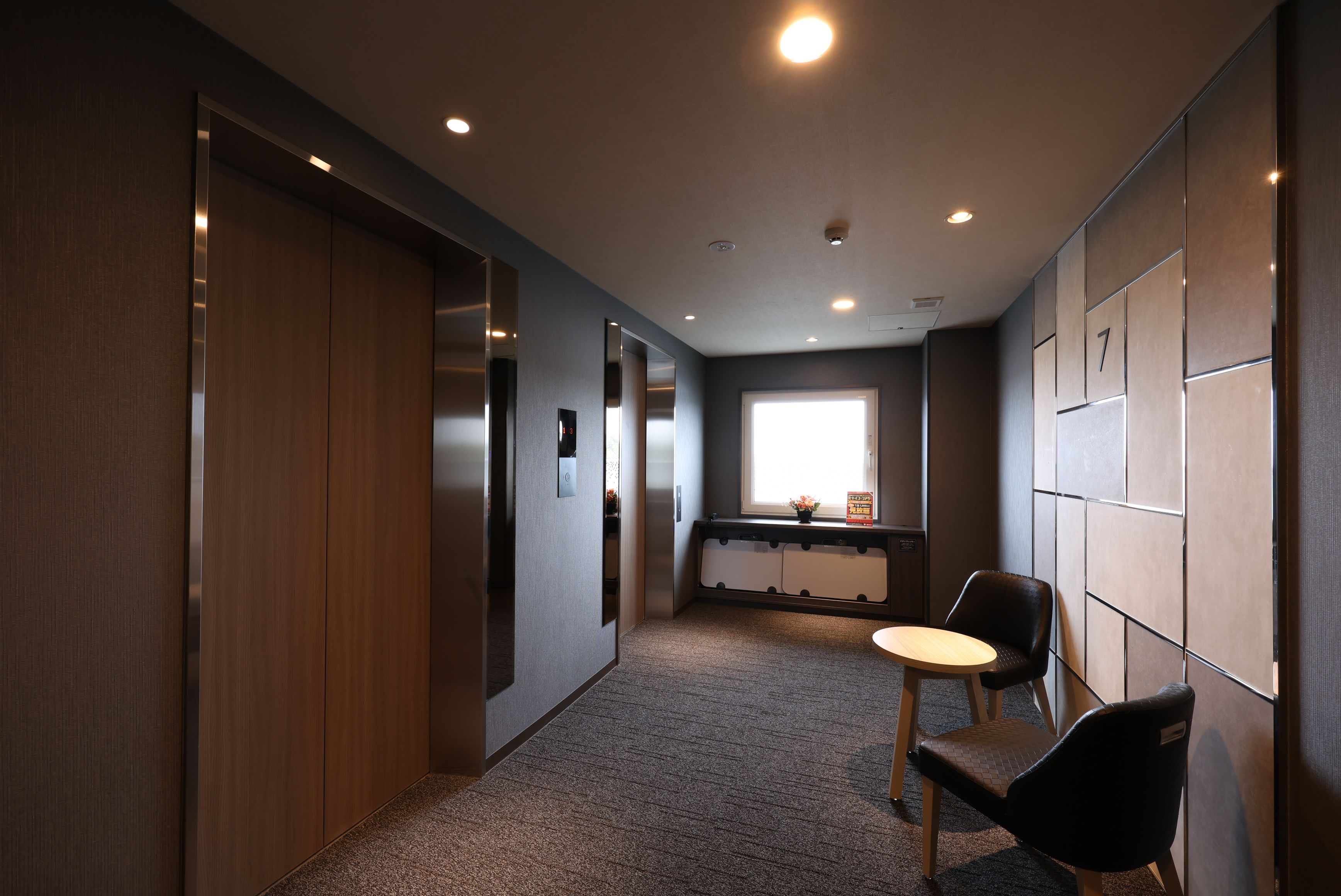 A hallway with a wooden door, a small table with a chair, and a window with natural light.