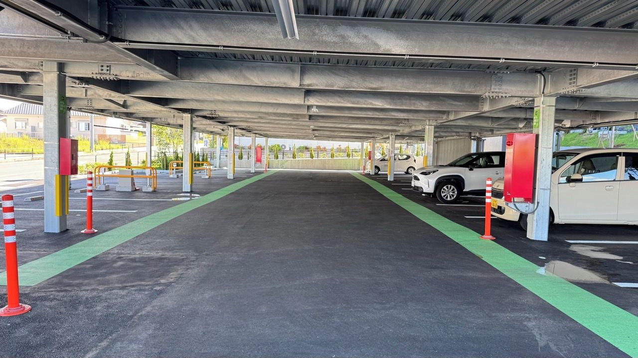 Ett överbyggt parkeringsområde med flera parkeringsplatser, en grön gångväg och staketstolpar.