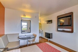 Habitación de hotel compacta con cama, una mesita, una silla, televisor y ventana con vista a un camión afuera.