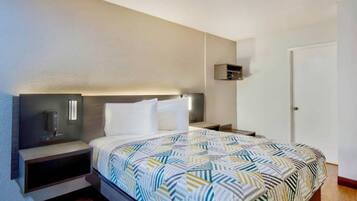 Una habitación de hotel con una cama, mesitas de noche, una lámpara de pared y una puerta.