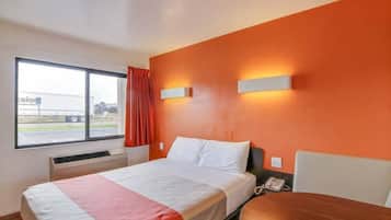A hotel room with a bed, a bedside table, a telephone, and a window with a view of a truck outside.