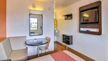A compact hotel room with a bed, a small table, a chair, a TV, and a window.