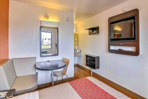 Une chambre d’hôtel de taille réduite, comprenant un lit, une petite table, une chaise, un téléviseur et une fenêtre.