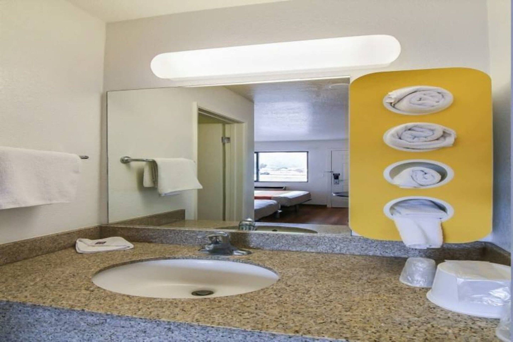 Baño de hotel con lavamanos de encimera de granito, un espejo y un perchero para toallas.