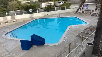 Piscina retangular com deck revestido, área de estar coberta e cerca delimitadora.