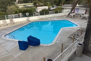 Piscina retangular com deck revestido, área de estar coberta e cerca delimitadora.
