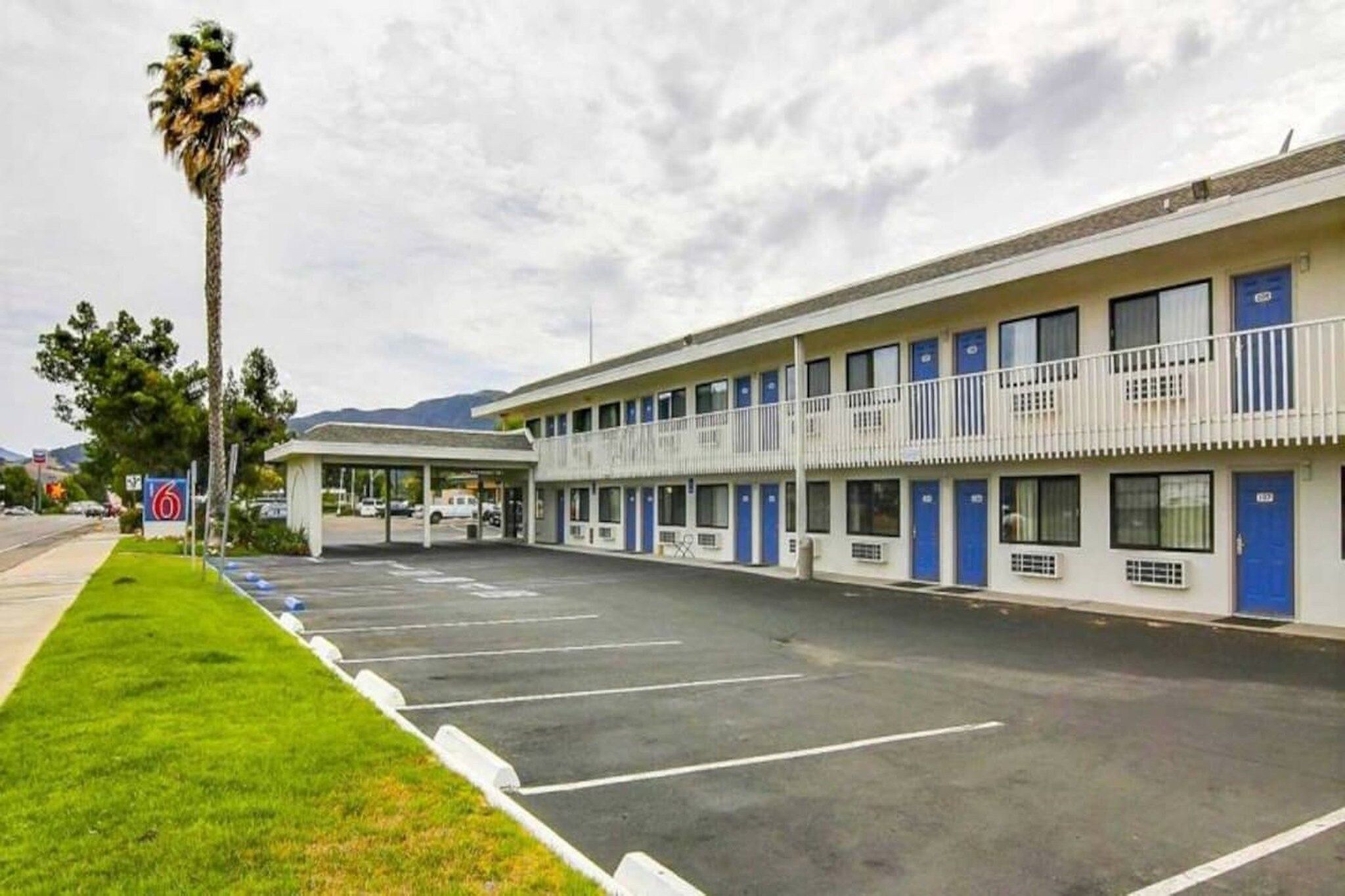 Um motel com estacionamento, área coberta e montanhas ao fundo.