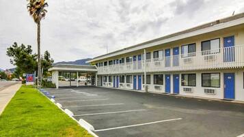 Um motel com estacionamento, área coberta e montanhas ao fundo.