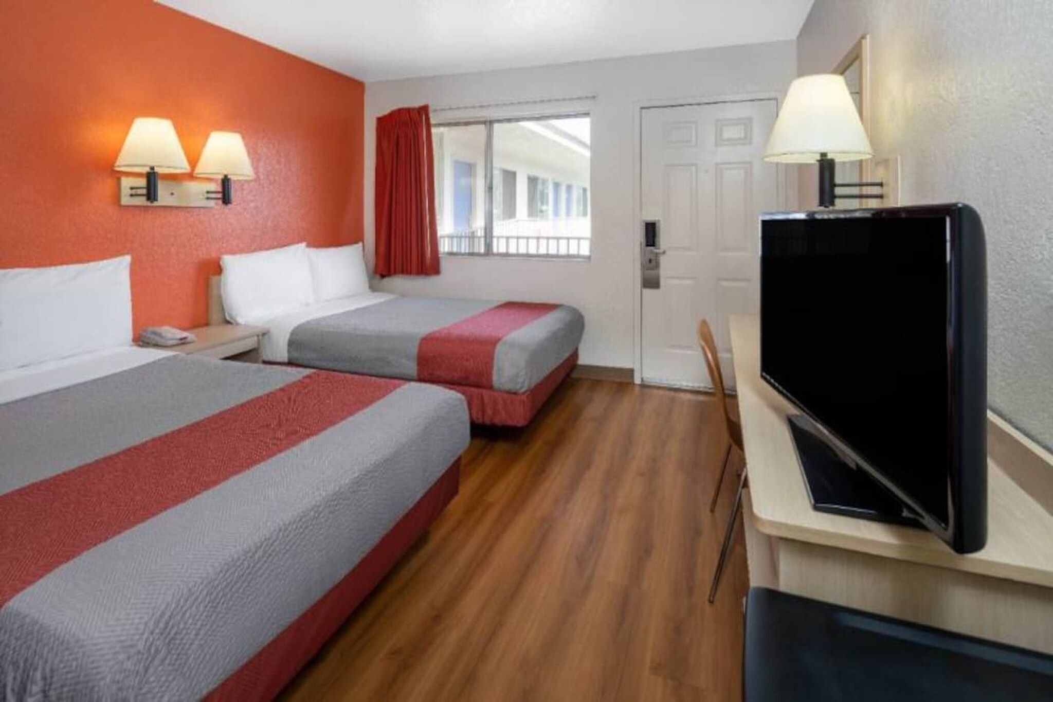Habitación de hotel con dos camas, televisión, escritorio y ventana con cortinas.