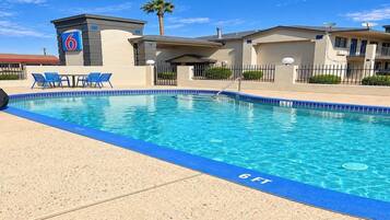 A swimming pool with a blue edge, a lounge area with chairs, and a building with a number sign.