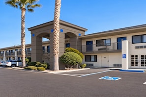 A hotel with a parking lot, a covered area, and a building with multiple floors and balconies.
