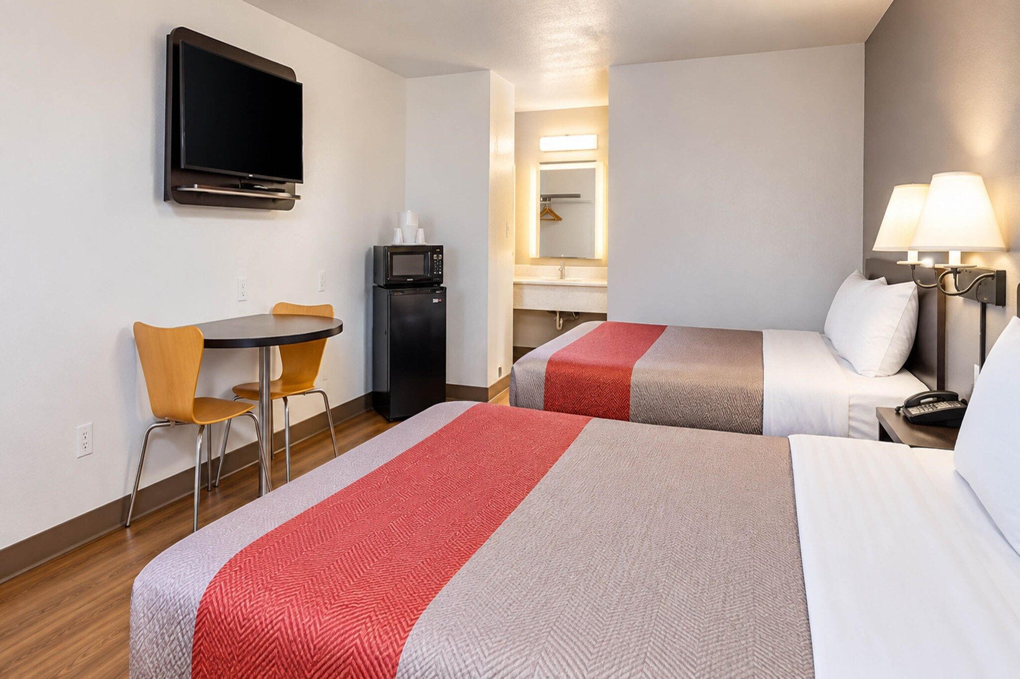 A hotel room with two beds, a desk, a chair, a television, a microwave, and a bedside lamp.