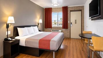 Habitación de hotel con cama, lámparas de noche, escritorio con silla, televisor montado en la pared y ventana con cortinas.