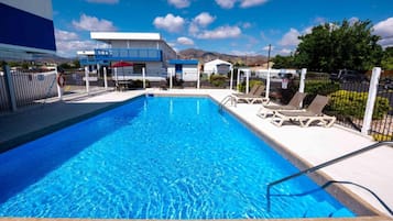 Una piscina con sillas de descanso, una silla de salvavidas y un edificio al fondo.