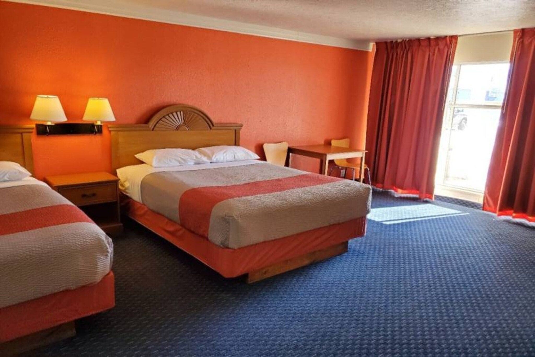 Habitación de hotel con una cama grande, dos mesitas de noche, una silla y un ventanal con cortinas.