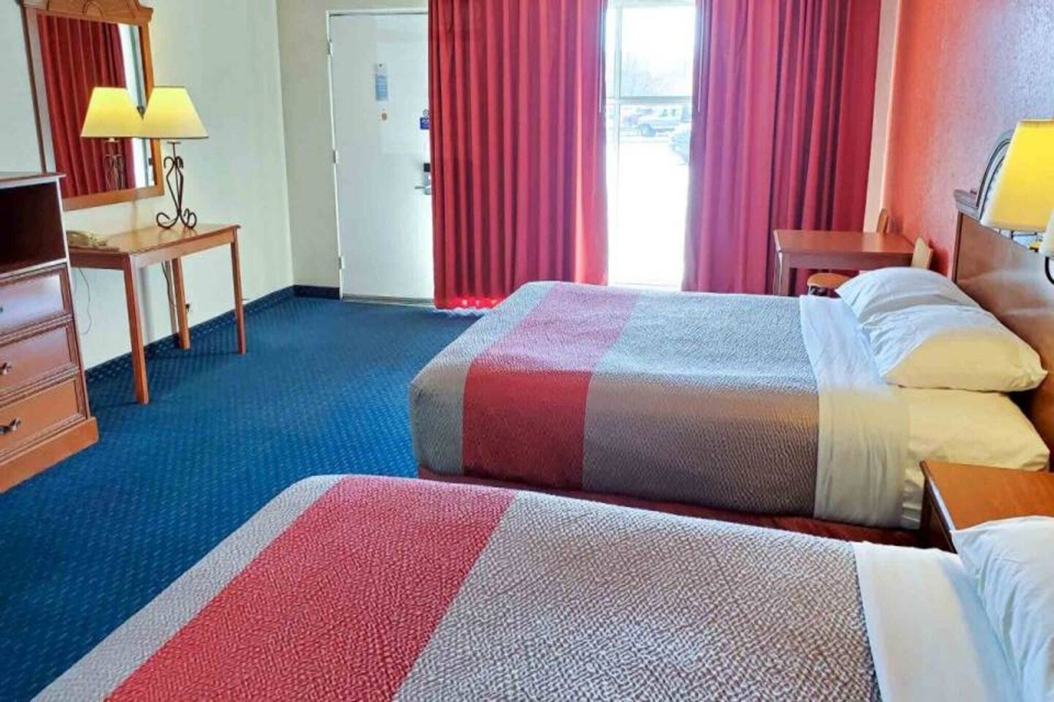Una habitación de hotel con dos camas, un escritorio, una lámpara y un armario.