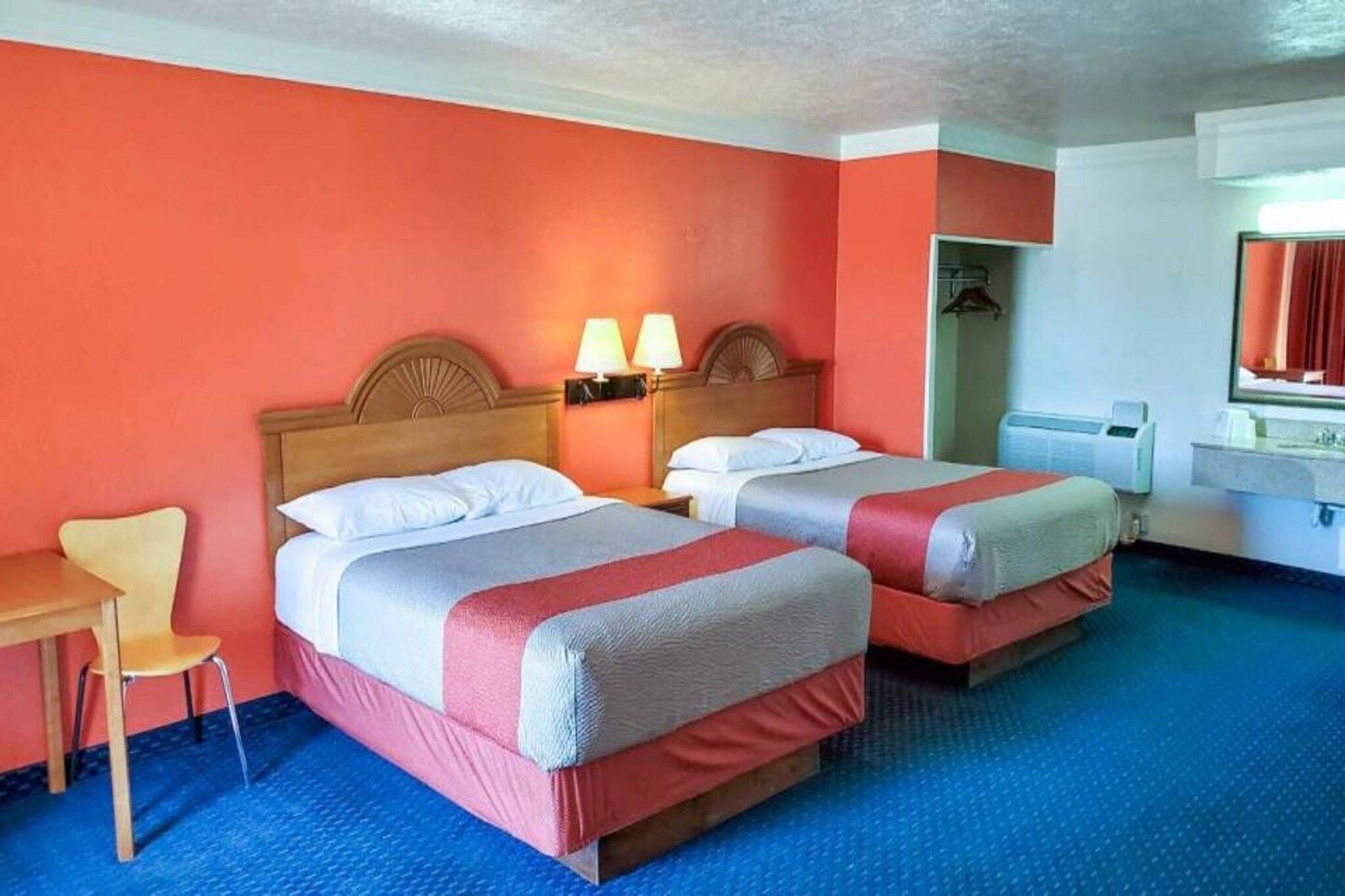 A hotel room with two beds, a desk, a chair, and a bathroom.