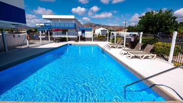 A swimming pool with lounge chairs, a lifeguard chair, and a building in the background.
