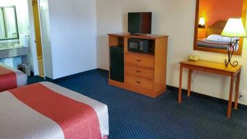 A hotel room with a bed, a wooden dresser with a television, a desk with a lamp, and a mirror.