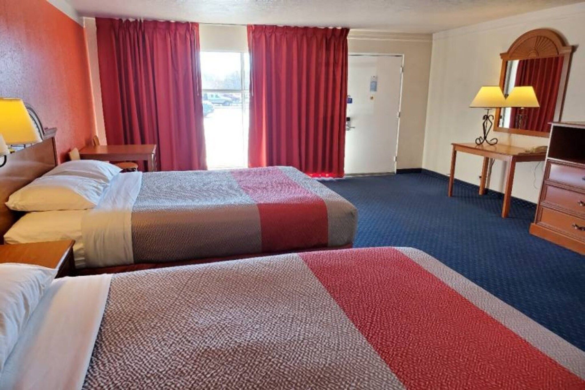 A hotel room with two beds, a desk, a chair, a dresser, and a window with curtains.
