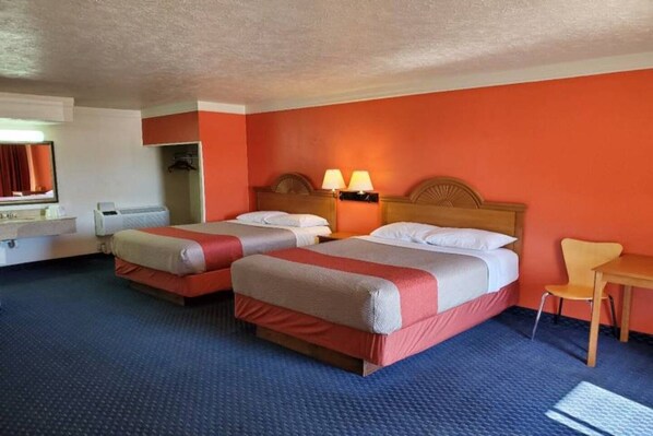 A hotel room with two beds, a desk, a chair, and a television.