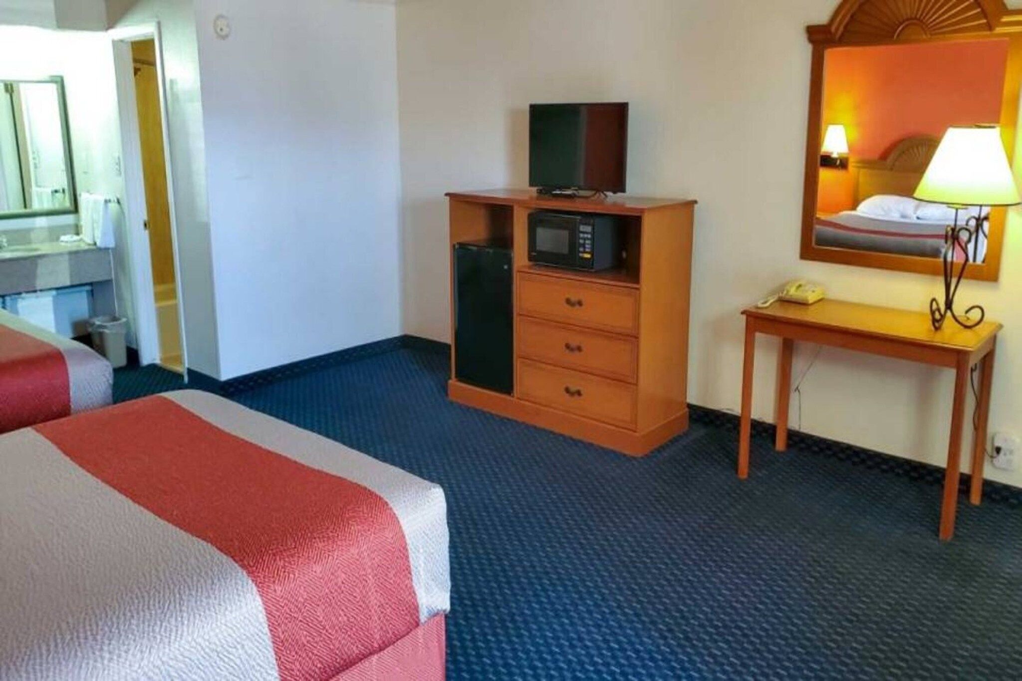 Et hotelværelse med seng, et trækommode med tv, et skrivebord med lampe og et spejl.