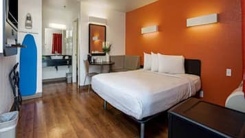 Een hotelkamer met een bed, een bureau, een stoel, een bijzettafeltje en een prullenbak.