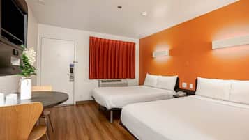 A hotel room with two beds, a desk, a chair, a vase with flowers, and a red curtain.