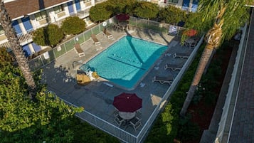 An aerial view of a hotel with a swimming pool surrounded by lounge chairs and umbrellas.