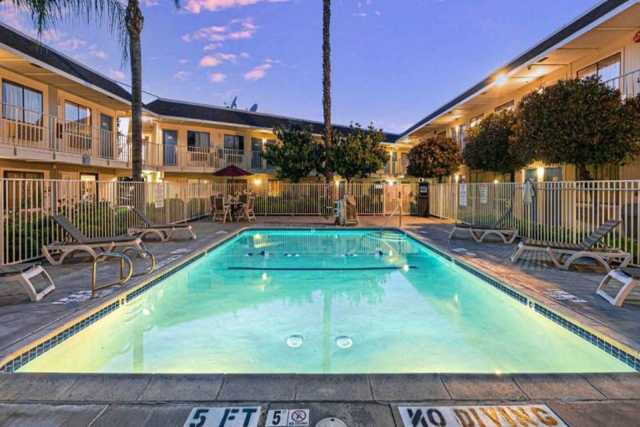 A swimming pool with a 5 ft depth marker, surrounded by lounge chairs and a fence.