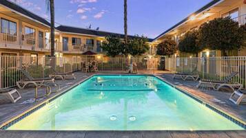 A swimming pool with a 5 ft depth marker, surrounded by lounge chairs and a fence.
