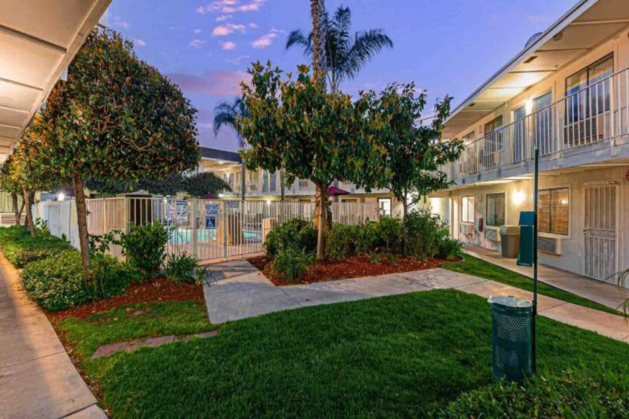 A hotel courtyard with a swimming pool, palm trees, and a well-maintained lawn.