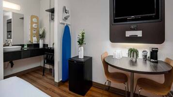 A hotel room with a bed, a desk with a coffee machine, a TV, and a small table with chairs.
