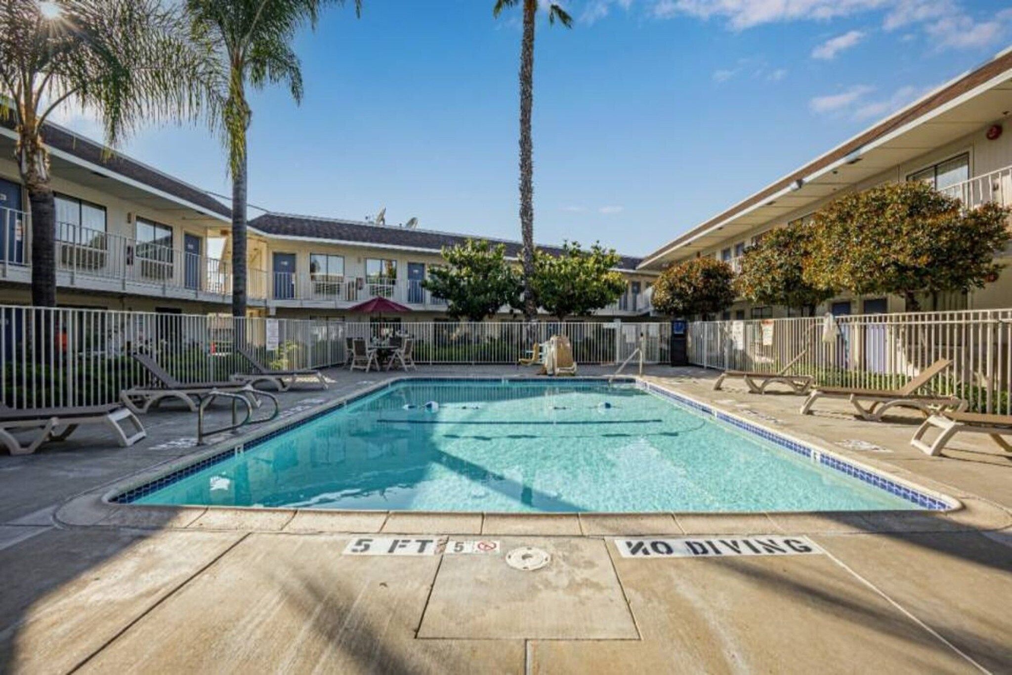 A swimming pool with a 'No Diving' sign, surrounded by lounge chairs and a fence.