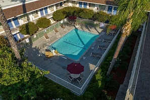 Vue aérienne d’un hôtel doté d’une piscine, entourée de chaises longues et de parasols.