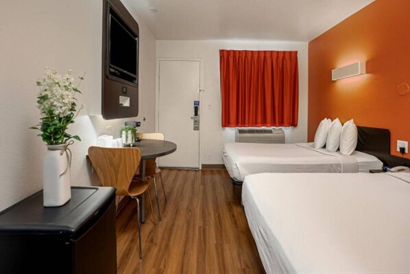 Habitació d'hotel amb llit, escriptori, cadira, televisió i finestra amb cortines.