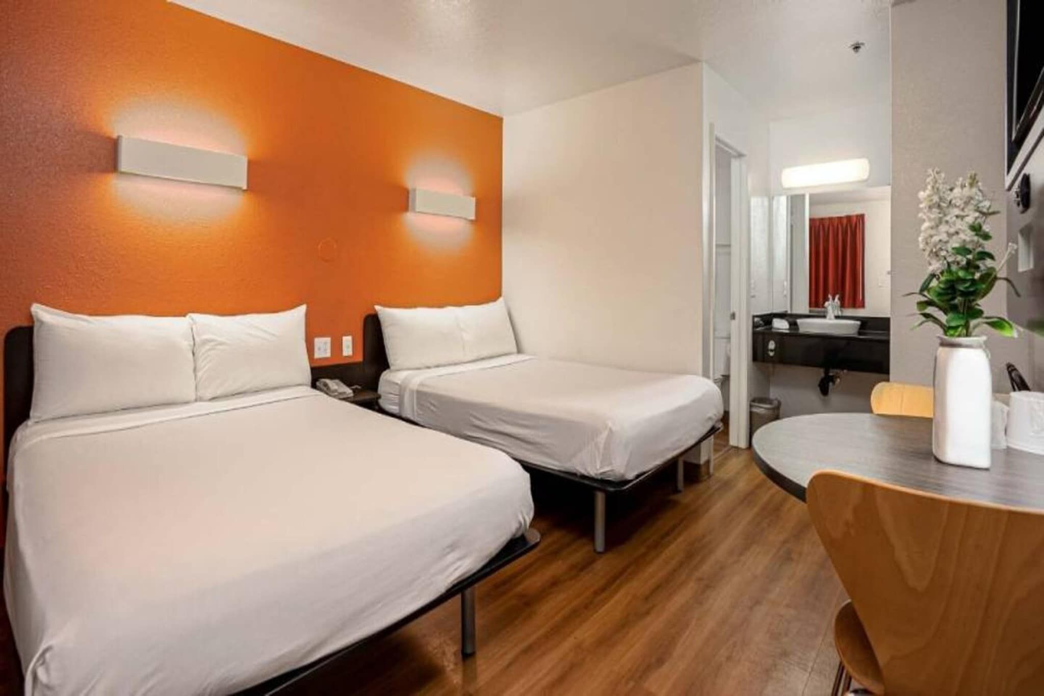 Ein Hotelzimmer mit zwei Betten, Holzboden, einem runden Tisch und einem durchgegangenen Türspalte erkennbaren Badezimmer.
