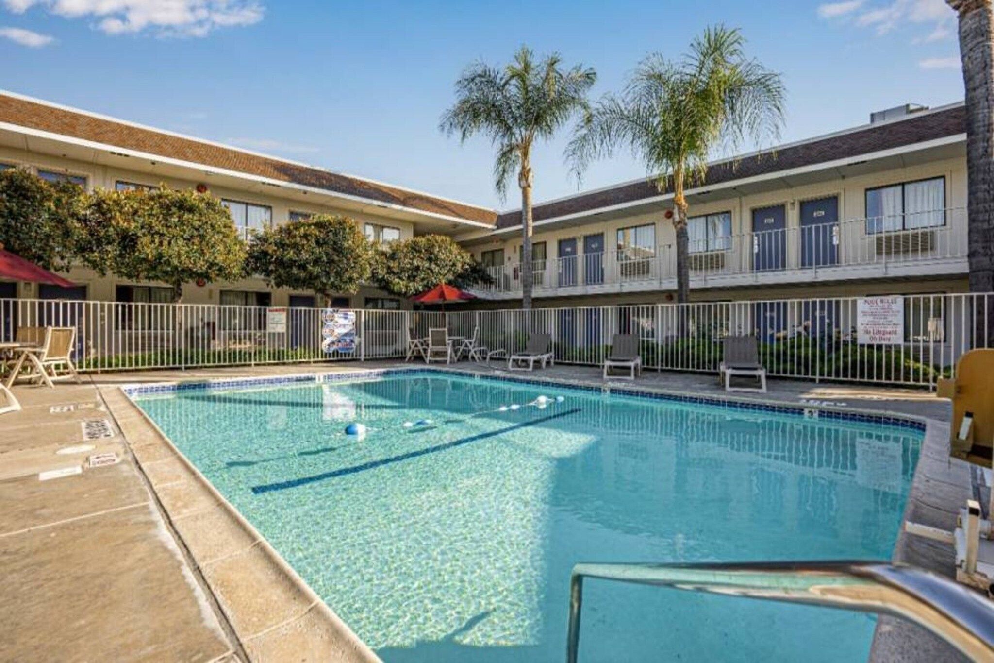 A swimming pool with lounge chairs and palm trees in a courtyard.