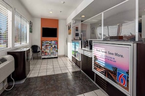 A hotel lobby with a reception desk, a magazine rack, and a large digital screen displaying a promotional message.