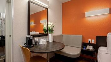 A hotel room with a round table, a chair, a sofa, a bedside table with a phone, and a mirror.