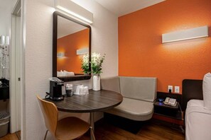 Habitació d'hotel amb una taula rodona, una cadira, un sofà, una cafetera, un vas amb flors i un mirall.