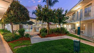 A hotel courtyard with a swimming pool, palm trees, and a well-maintained lawn.
