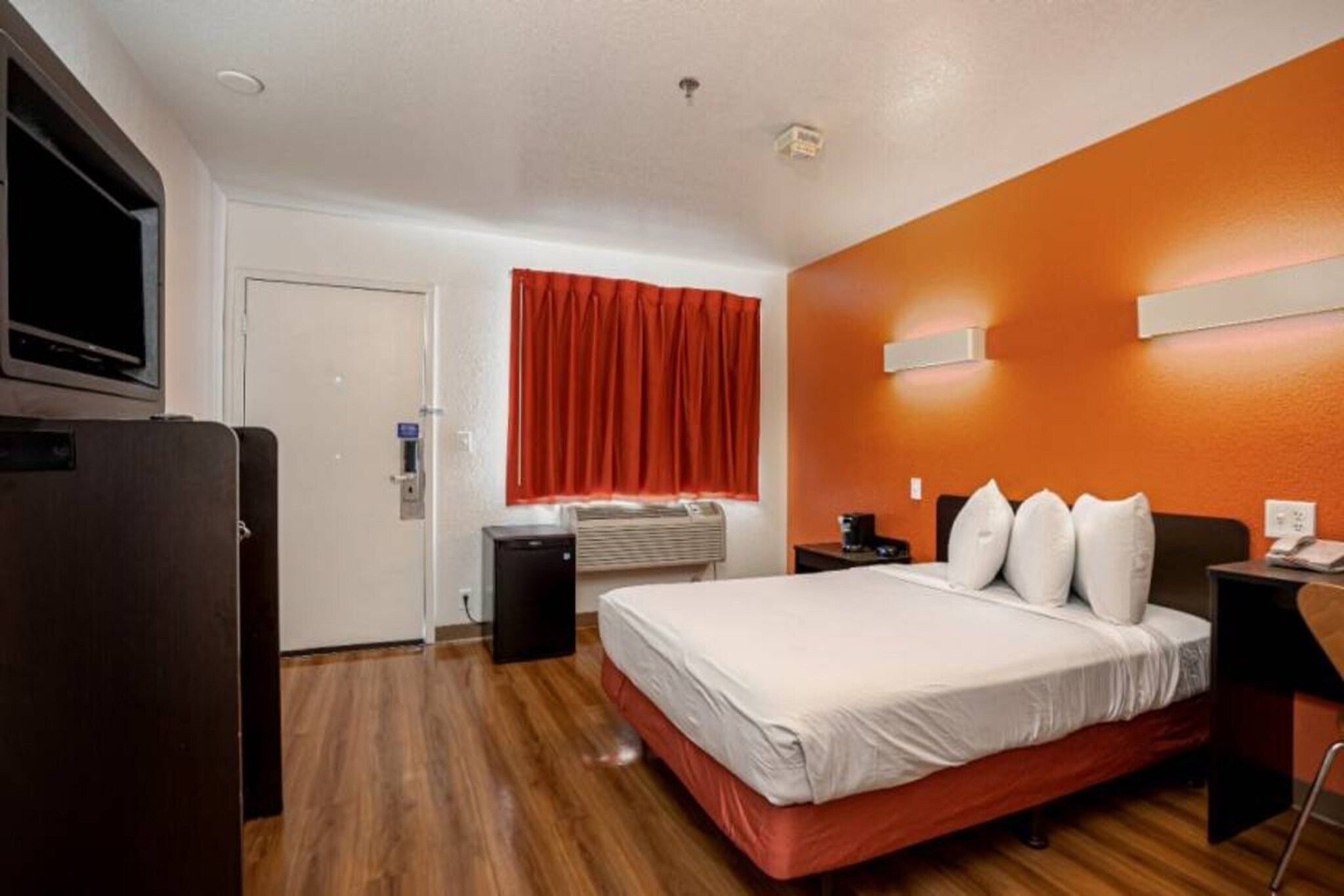 A hotel room with a bed, a TV, a heater, and a red curtain.