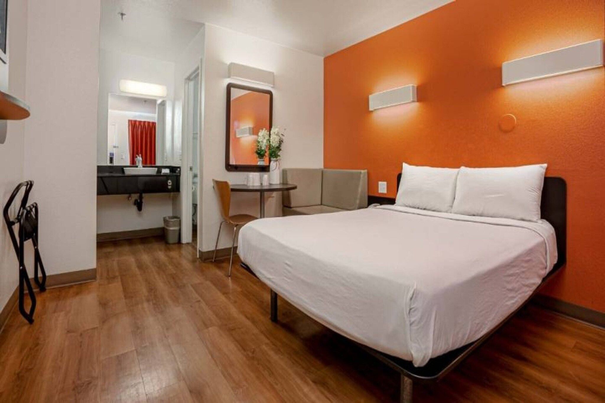 A hotel room with a bed, a desk, a chair, a mirror, and a bathroom.