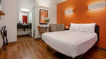 A hotel room with a bed, a desk, a chair, a mirror, and a bathroom.
