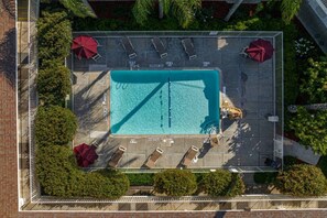 An aerial view of a rectangular swimming pool with lounge chairs and umbrellas, surrounded by a fence and greenery. - 1 Queen Bed | Premium, Mini Fridge (Temecula)