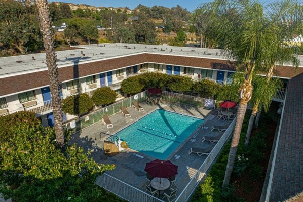 A rooftop pool with lounge chairs and umbrellas, surrounded by a fence and palm trees. - 1 Queen Bed | Premium, Mini Fridge (Temecula)